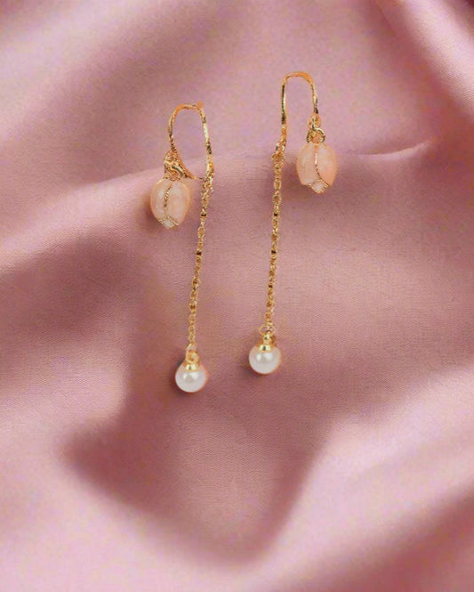 Pair of gold earrings with pink stones on a textured brown surface