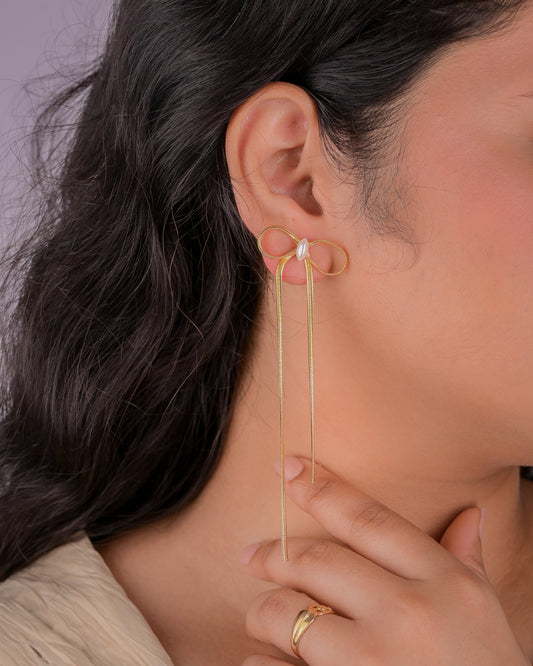 Gold earring worn by a person with dark hair, against a neutral background
