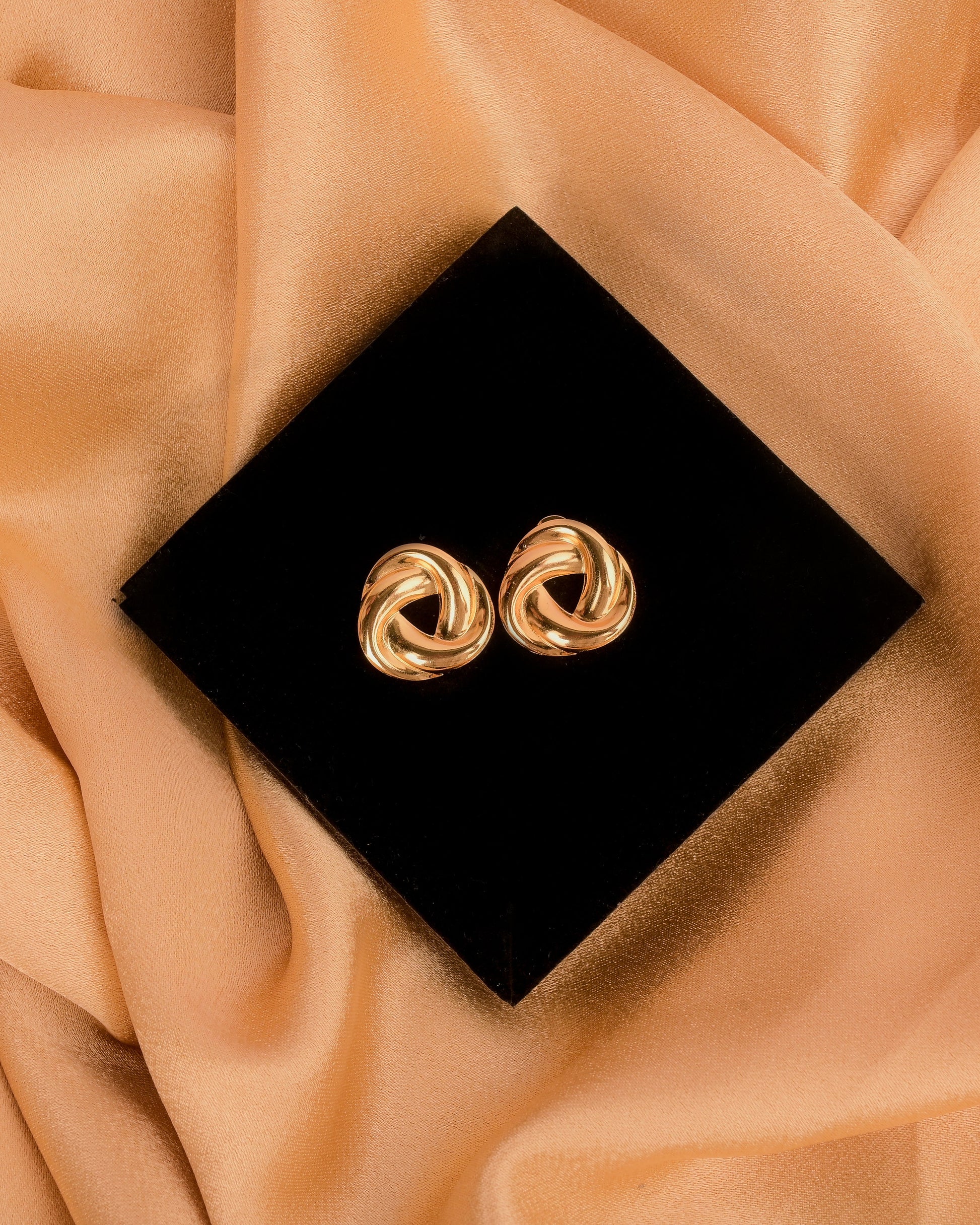 Gold earrings on a black box with a beige fabric background