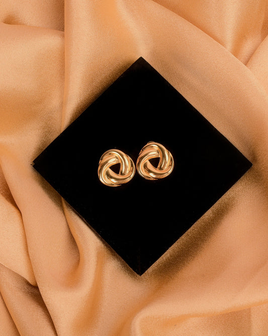 Gold earrings on a black box with a beige fabric background