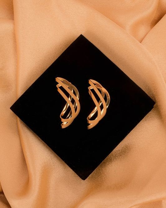 Gold earrings on a black square box with beige fabric background