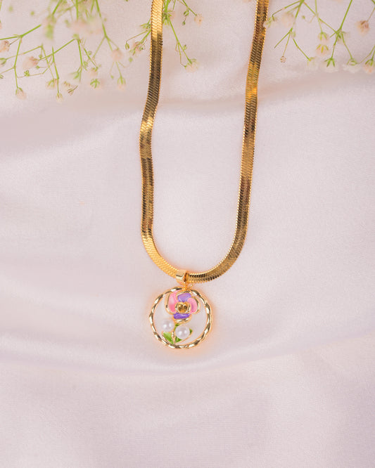 Gold necklace with a floral pendant on a light pink background