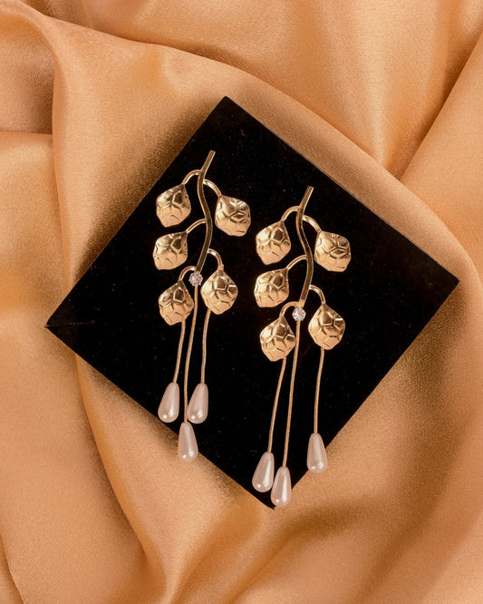 Gold earrings on a black stand with beige fabric background