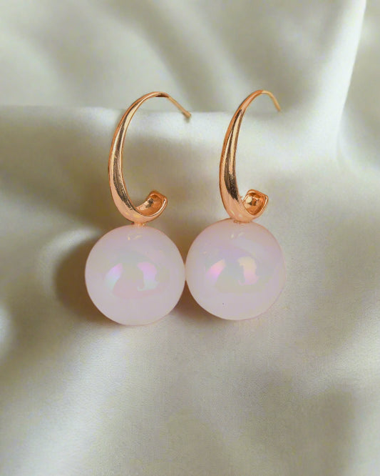 Gold hoop earrings with white pearls on a textured brown and white background