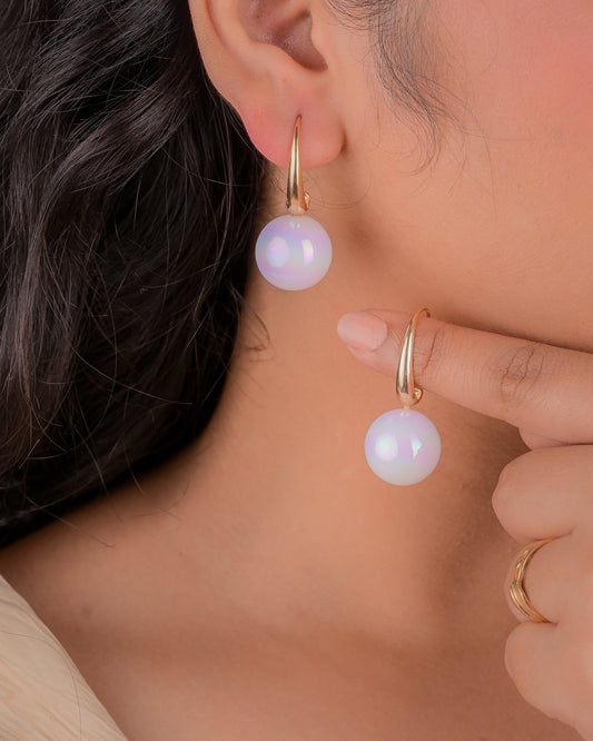 Close-up of a woman wearing gold hoop earrings with purple gemstones.
