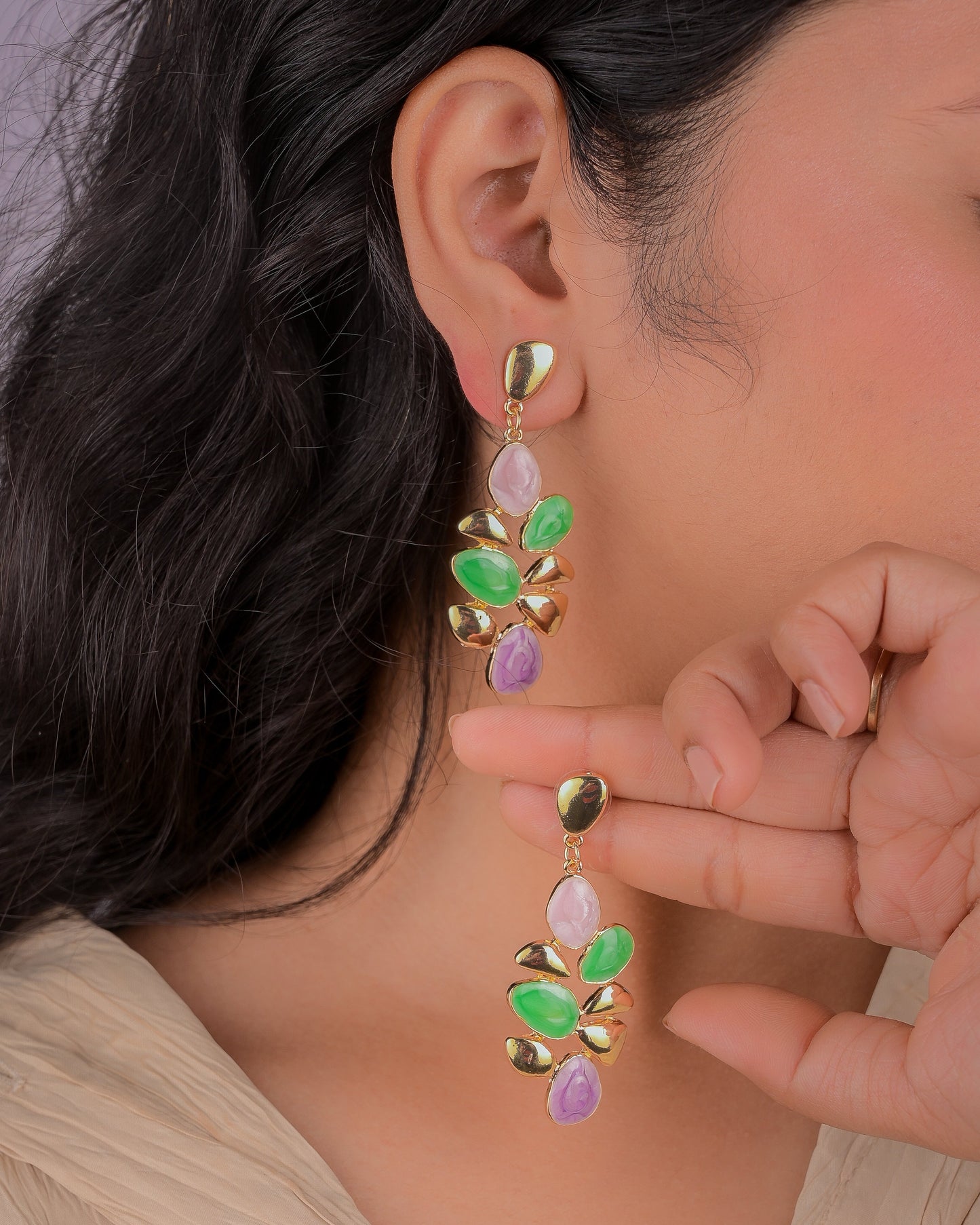 Close-up of a person wearing a gold earring with green and purple stones.