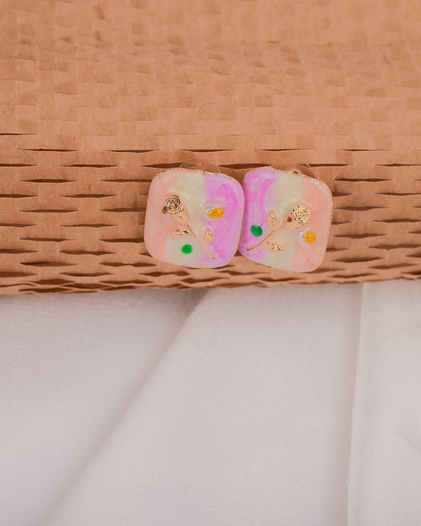 Pair of pink earrings with floral designs on a woven surface