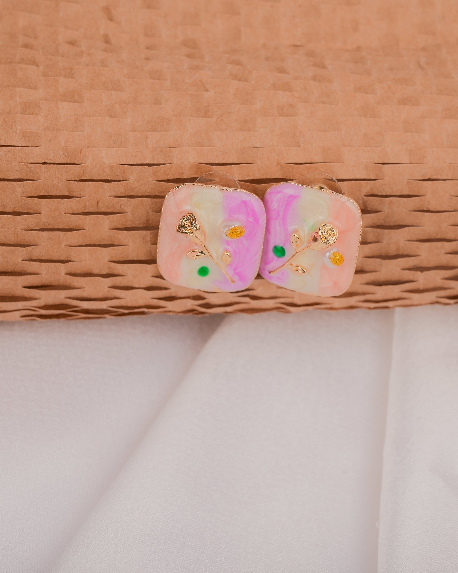 Pair of pink earrings with floral designs on a woven surface