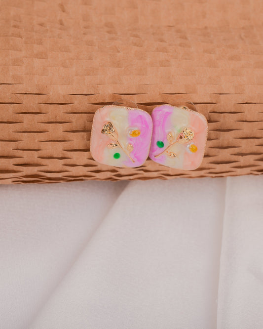 Pair of pink earrings with floral designs on a woven surface
