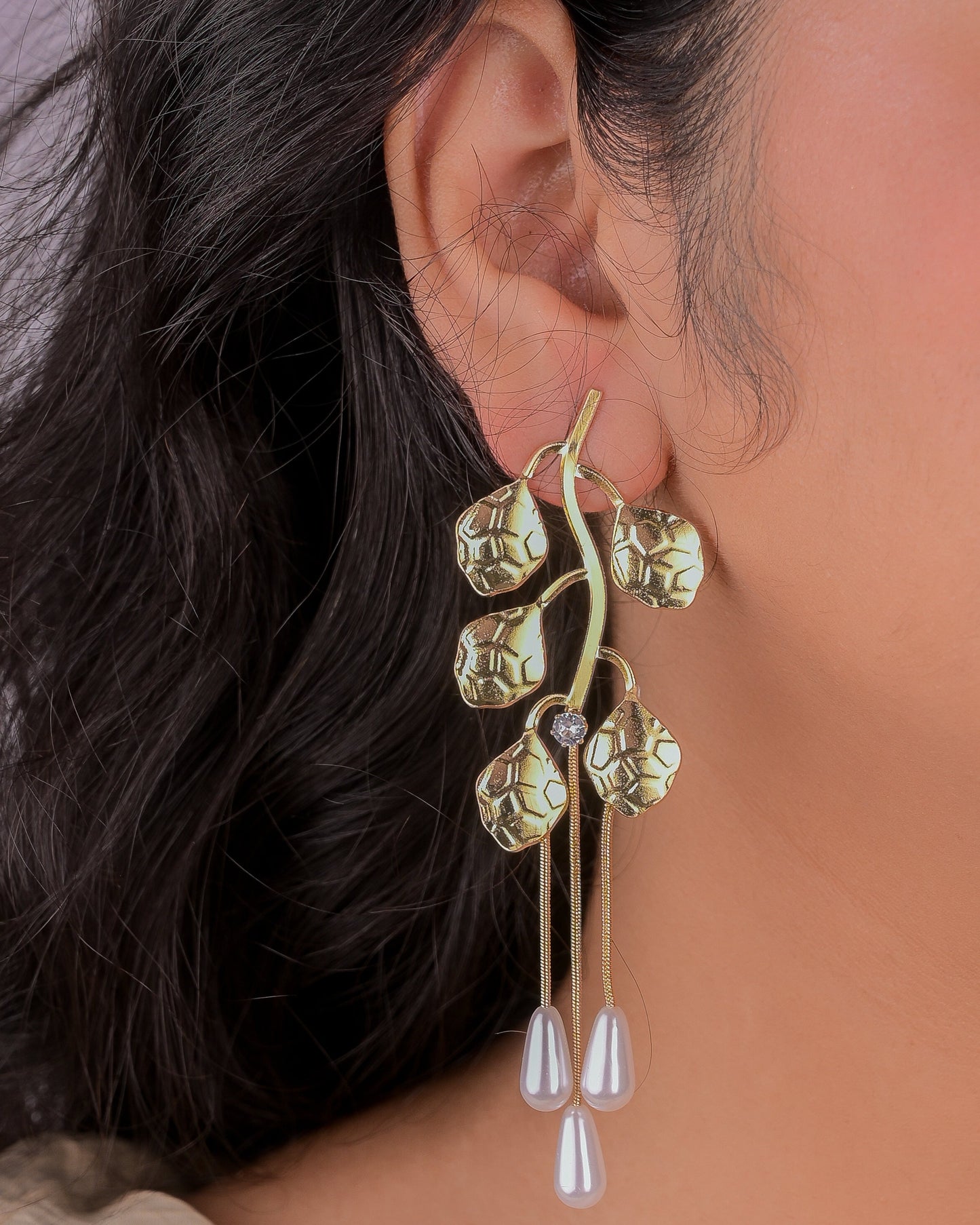 Close-up of a person wearing a gold and pearl earring with a blurred background