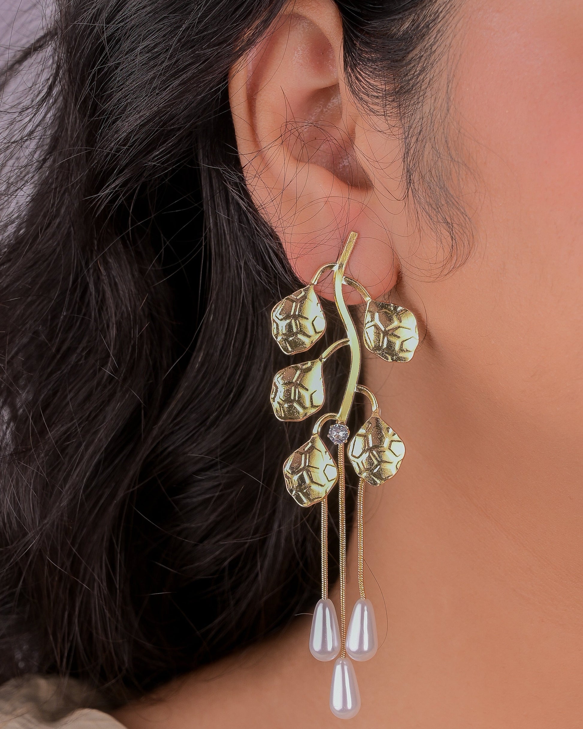 Close-up of a person wearing a gold and pearl earring with a blurred background