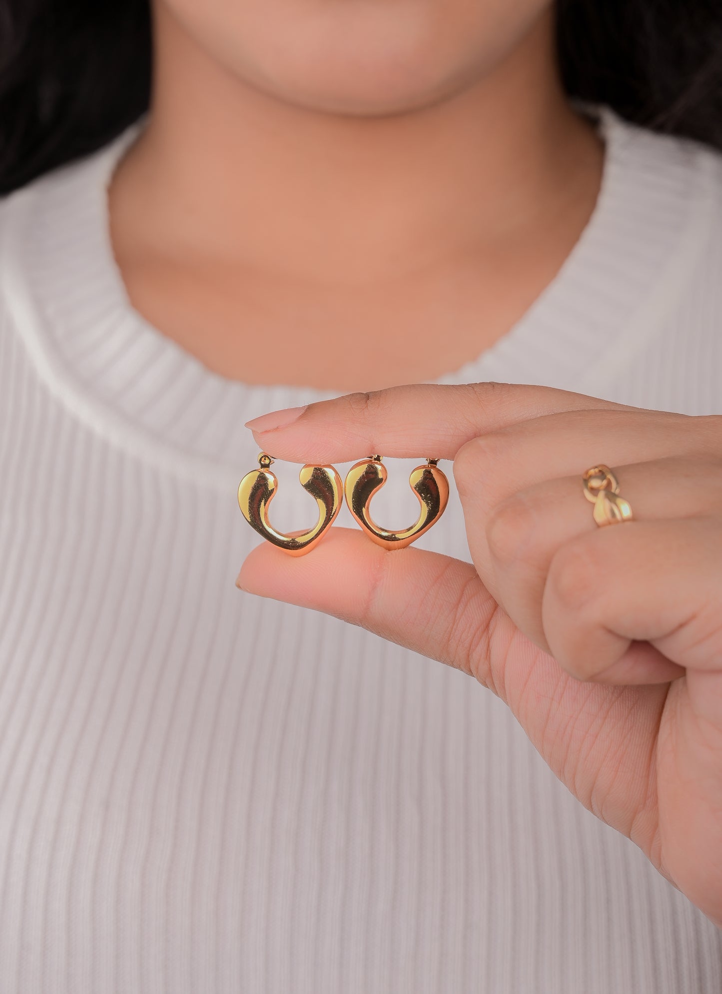 Gold hoop earrings held by a person wearing a white sweater.