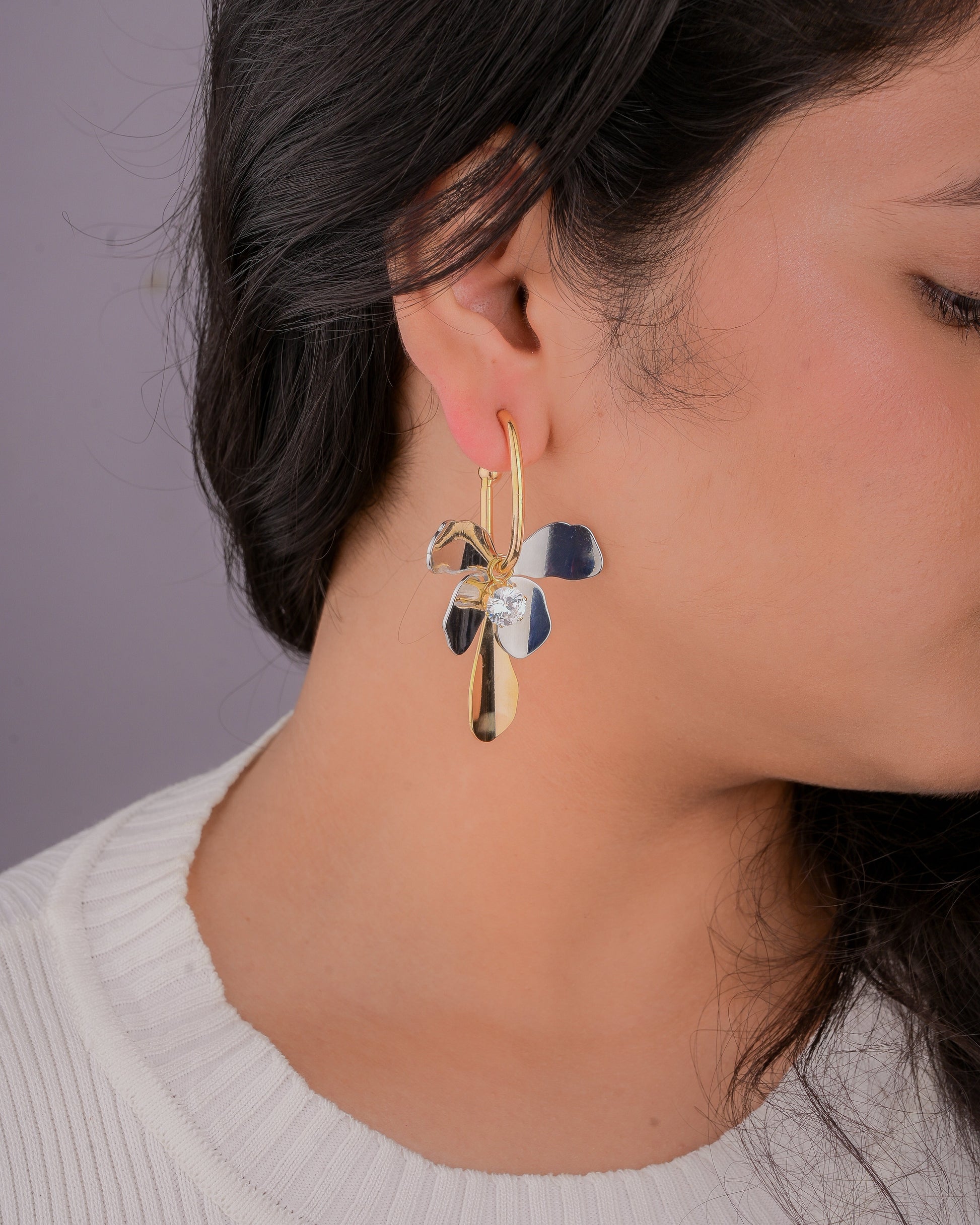 Close-up of a person wearing a gold and silver earring against a neutral background