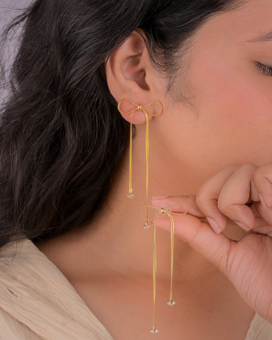 Gold bow-shaped earrings worn by a person with a neutral background